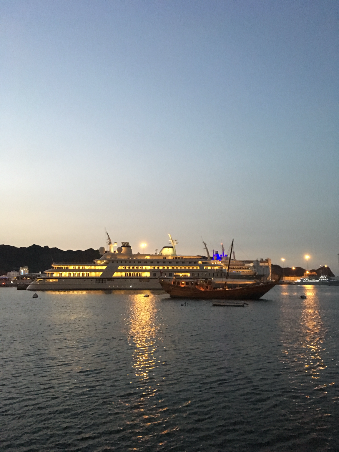 Illuminated yacht and traditional wooden dhow in Muscat harbour at dusk